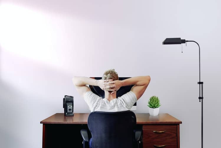 a man working on his desk with hands behind his head