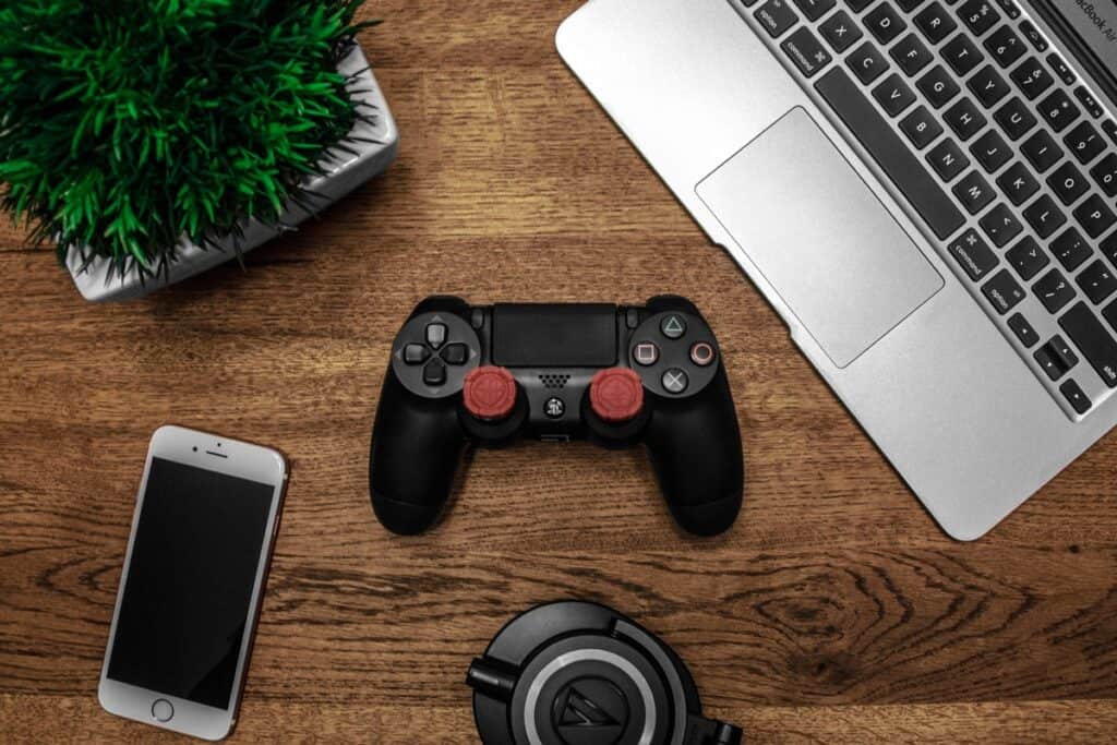 A laptop, iPhone, and a game controller placed together on a table. How to Code a Game
