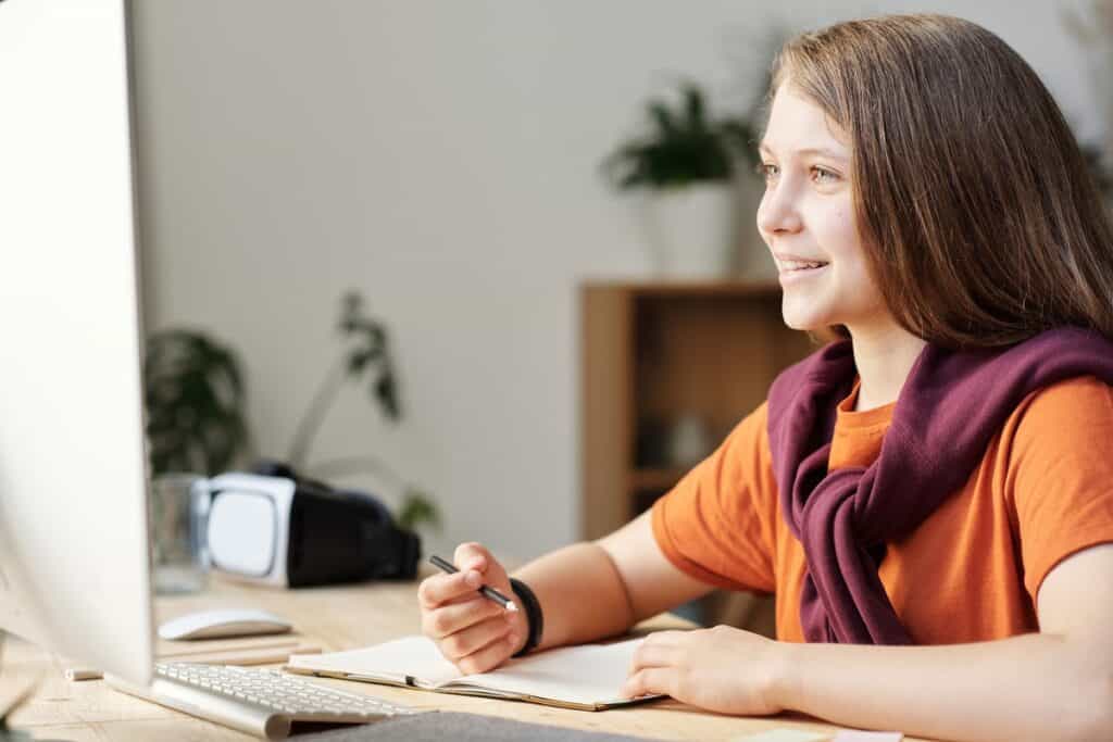 Girl taking notes while smiling at her computer screen Studying Computer Science Before College