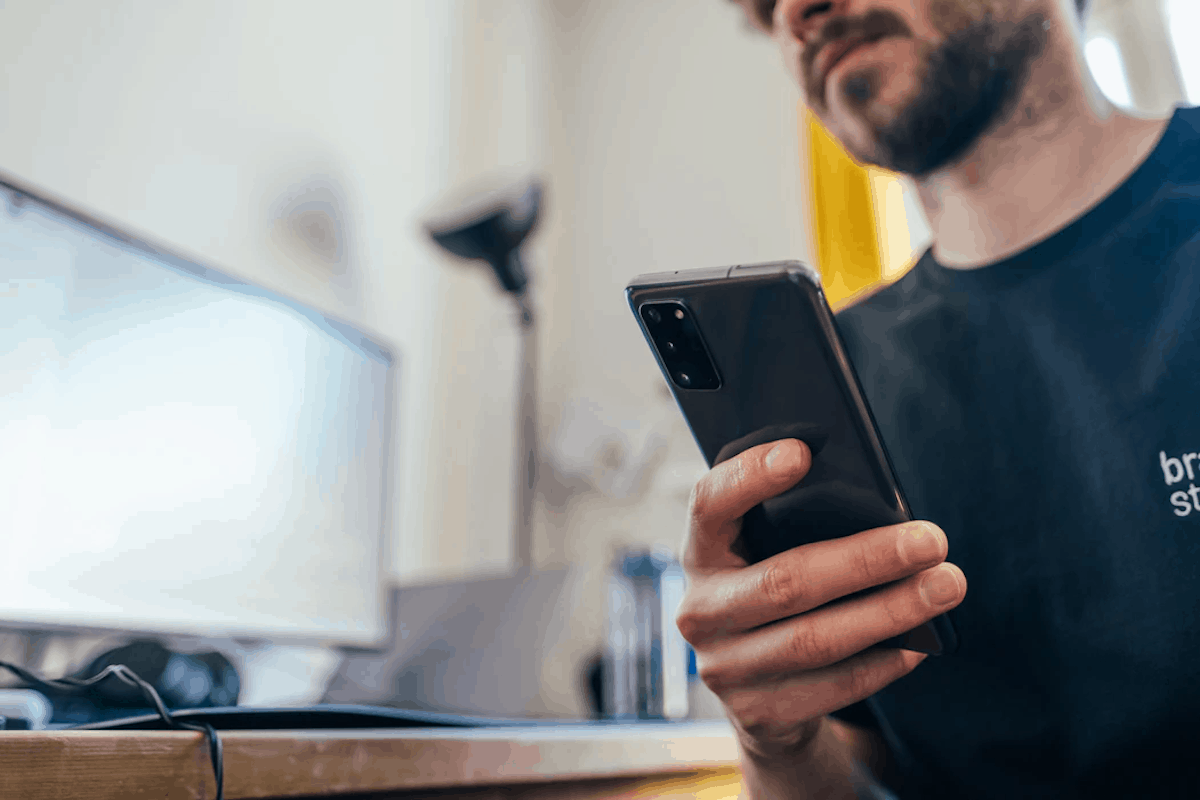 Person holding a phone in one hand in front of a desktop computer top coding apps for beginners