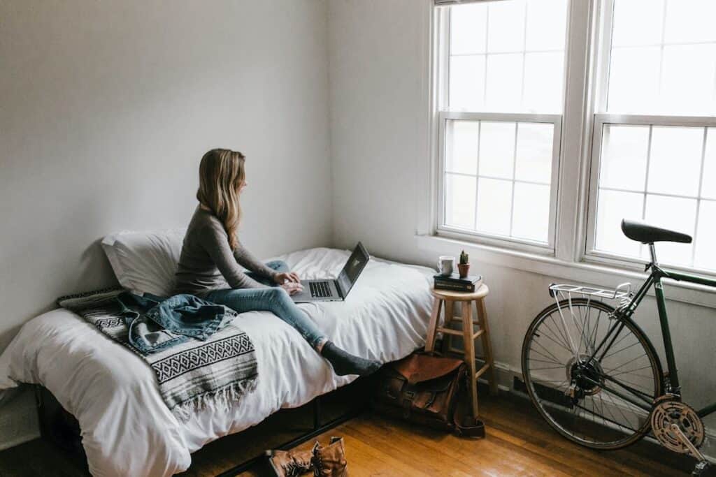 Young woman in a grey shirt sitting with her laptop on a bed guide to highschool equivalency exams