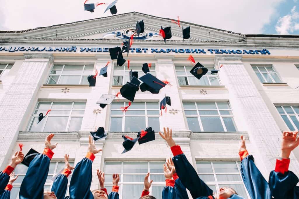 A group of graduates throwing their graduation caps in the air. Coding Bootcamp vs College
