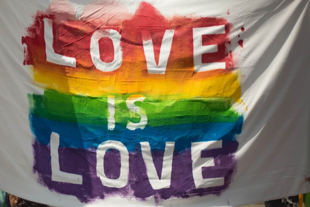 A white flag painted with a rainbow and the phrase “love is love”. LGBTQ+ Coding Bootcamp Scholarships