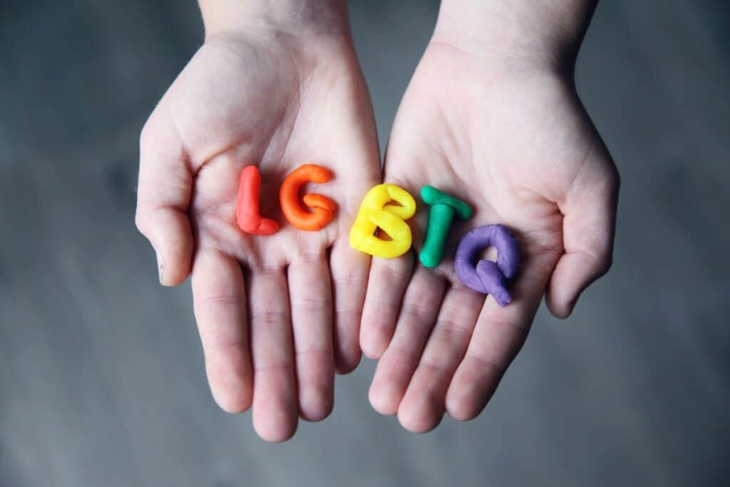Two hands holding the rainbow letters spelling LGBTQ. LGBTQ+ Coding Bootcamp Scholarships