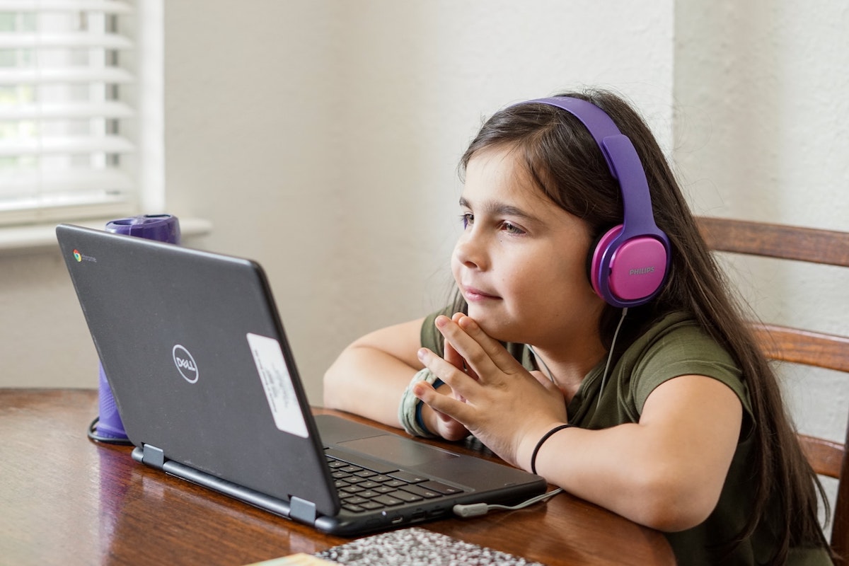 A young girl sitting at a table watching computer animation tutorials on her laptop.