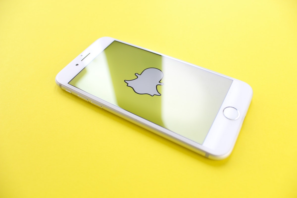 White iPhone with screen-sized Snapchat logo on a yellow background