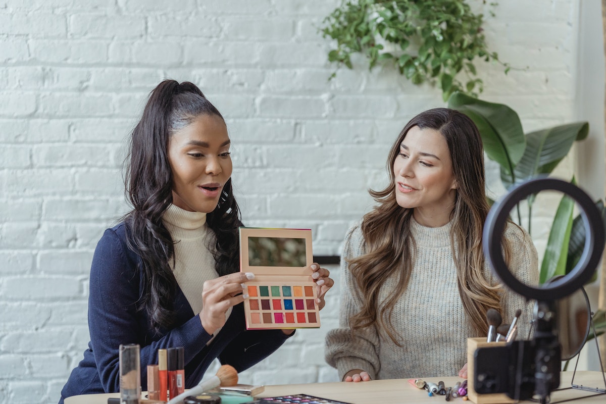 Young diverse ladies recording vlog about makeup products on smartphone