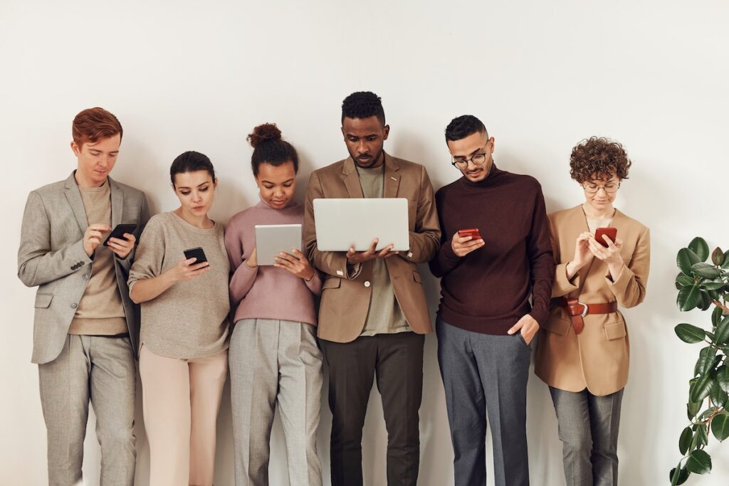 A group of six professional young adults all holding and looking at different devices.
