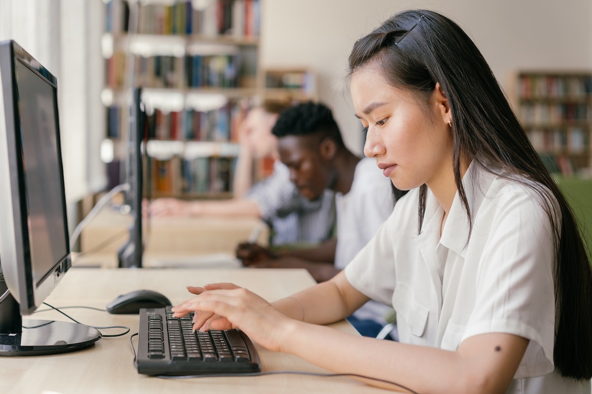 A college student works in a computer lab, typing on a desktop computer.