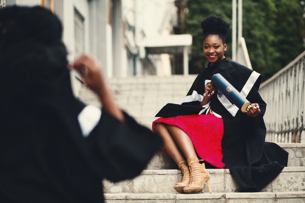 A college graduate sitting on the stairs of her institution. 
