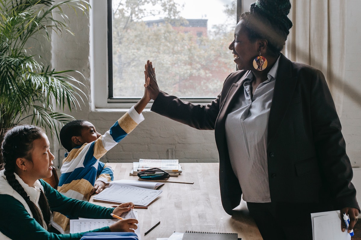 A female teacher giving high five to schoolkids in classroom.