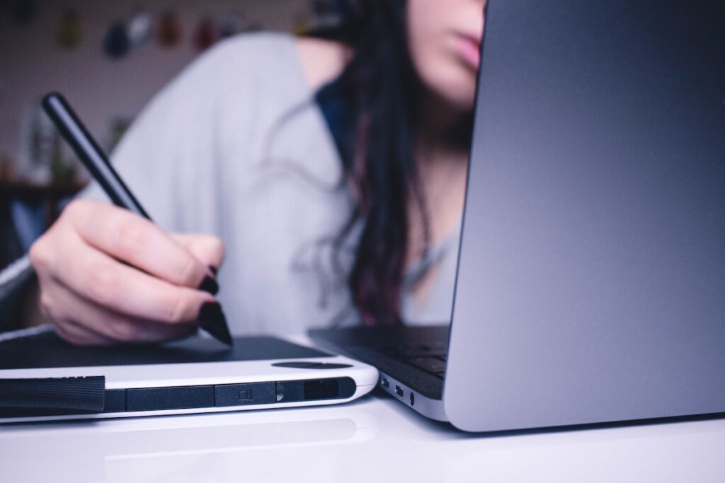 A girl holding a stylus pen and working on a laptop
