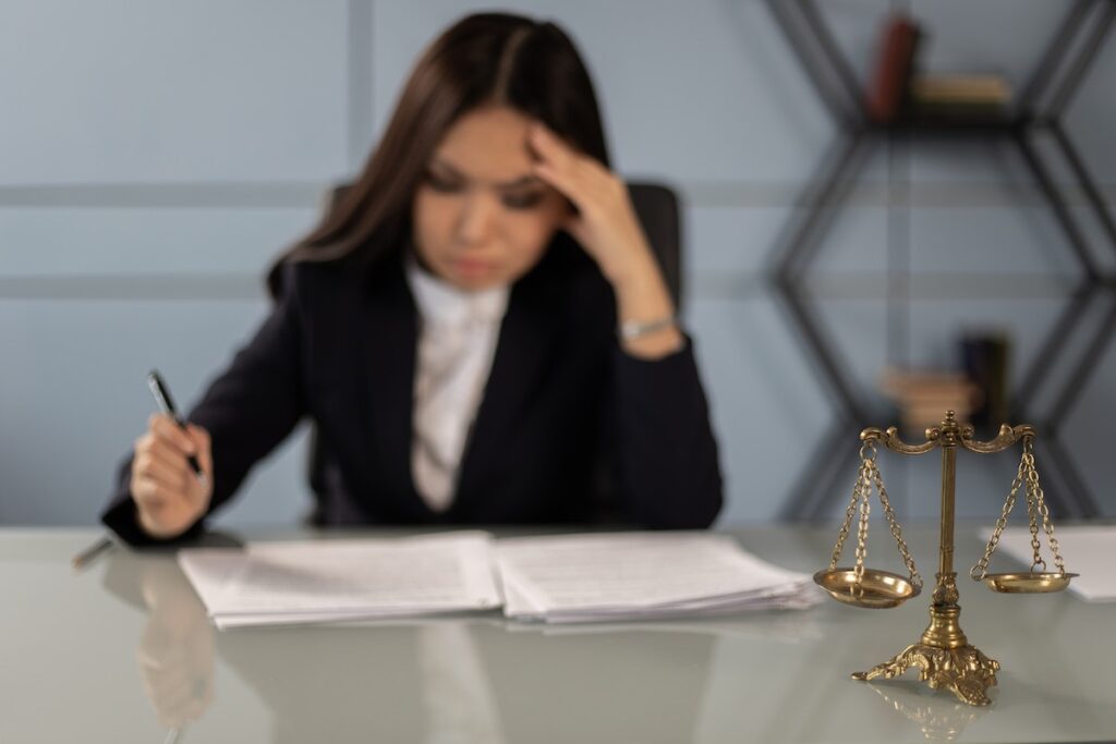 A female lawyer doing some paperwork with scales of justice on the desk.