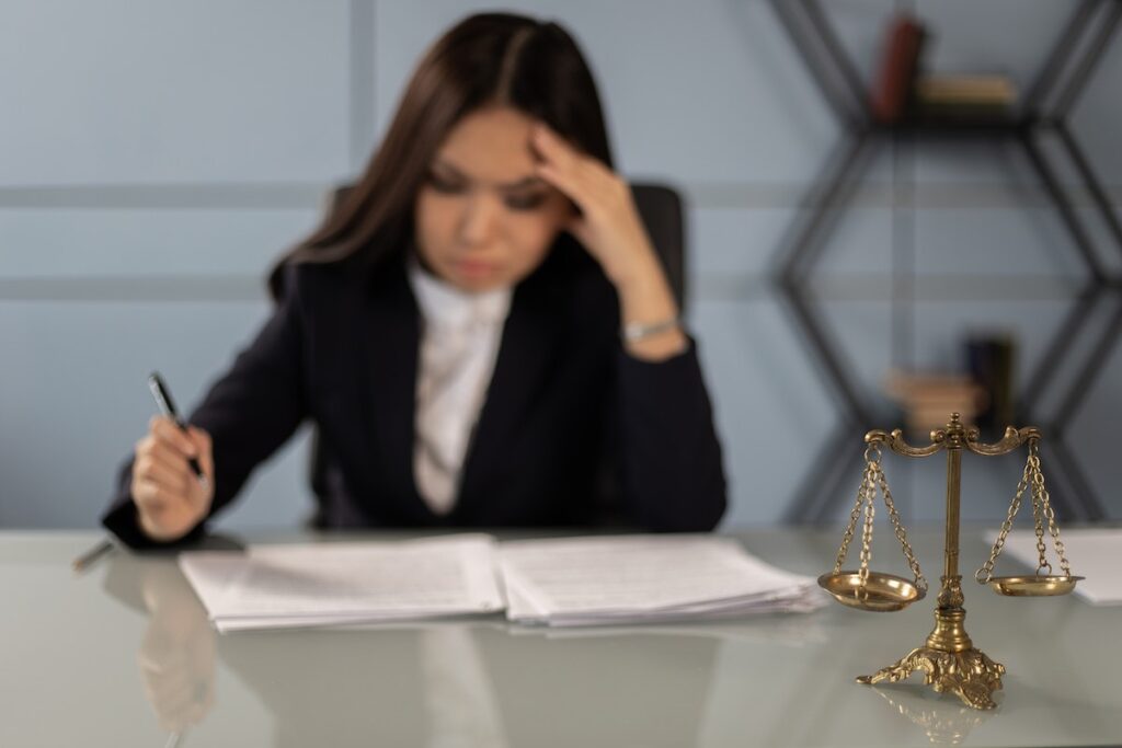 A female lawyer doing some paperwork with scales of justice on the desk.
