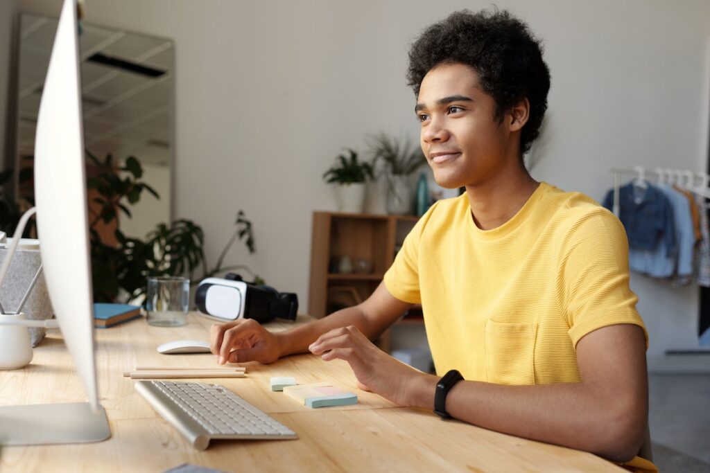 A man in a yellow shirt is using a white desktop computer.
